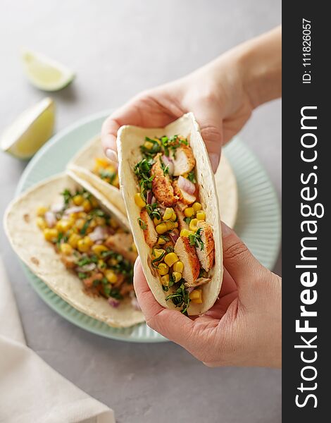 Hands holding tacos with roasted chicken meat, corn, parsley, salsa and sweet pepper.