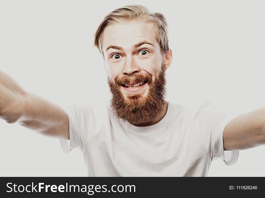 Close up portrait of a cheerful bearded man taking selfie over white background. Studio shoot.