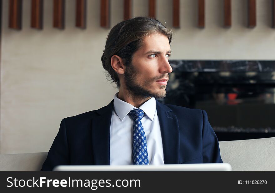 Young businessman working on laptop, sitting in hotel lobby waiting for someone.