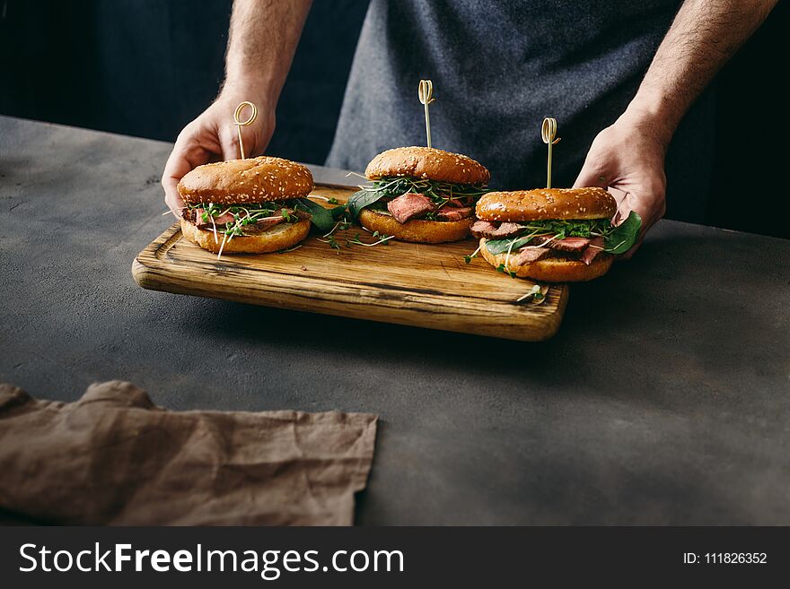 Man holding on cutting board set burger with beef medium rare, spinach, green sauce and micro greens. Man holding on cutting board set burger with beef medium rare, spinach, green sauce and micro greens