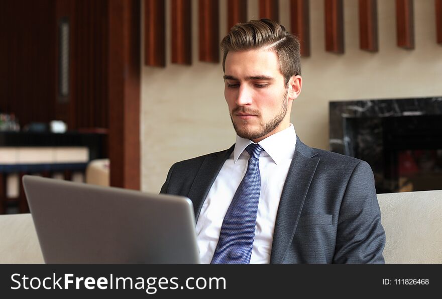 Young businessman working on laptop, sitting in hotel lobby waiting for someone.