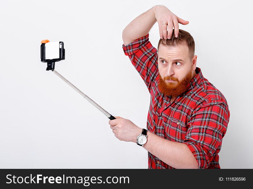 Man with red beard in plaid shirt makes selfie on phone. Man with red beard in plaid shirt makes selfie on phone