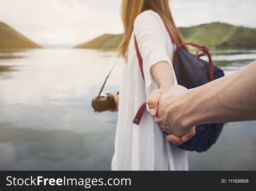 Young woman with camera holding man`s hand and leading him on nature outdoor, Couple vacation travel