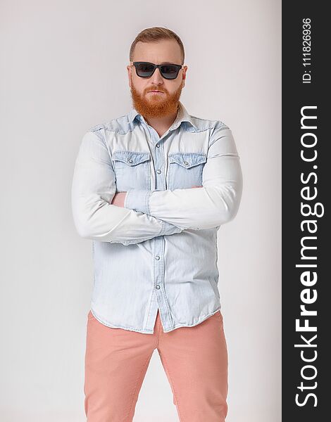 Smiling red-haired beard man in sunglasses and denim shirt on gray background.