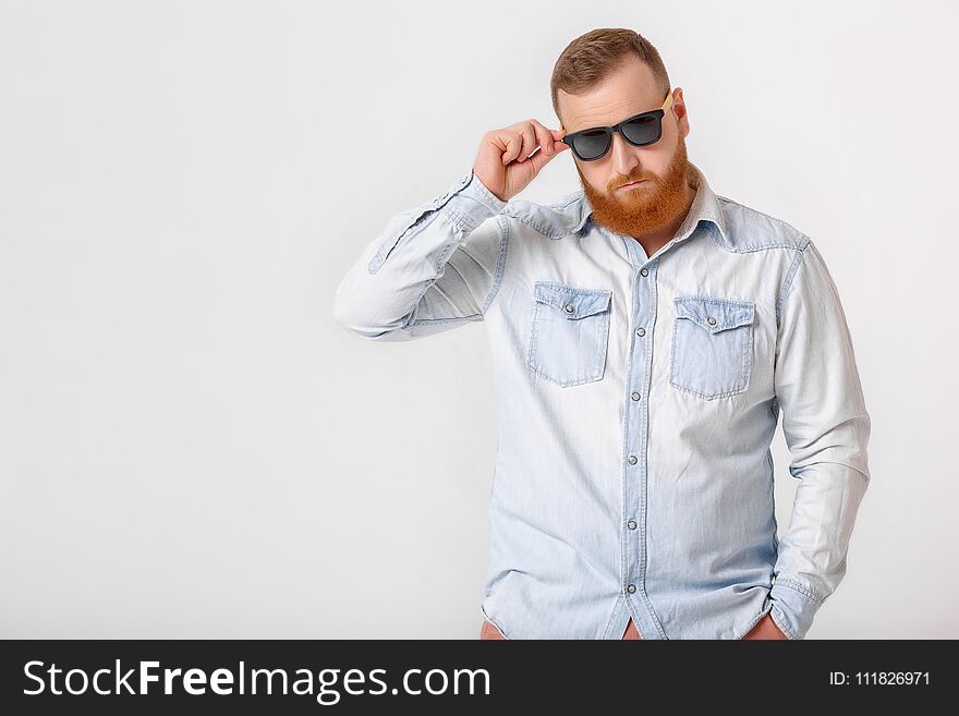 Smiling red-haired beard man in sunglasses and denim shirt on gray background. copy space
