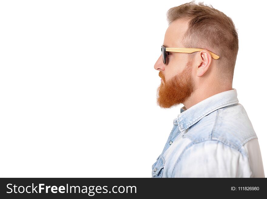 Profile of red-haired beard man in sunglasses and denim shirt on gray background.