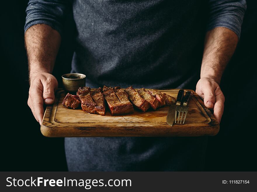 Man holding juicy grilled beef steak with spices on cutting board