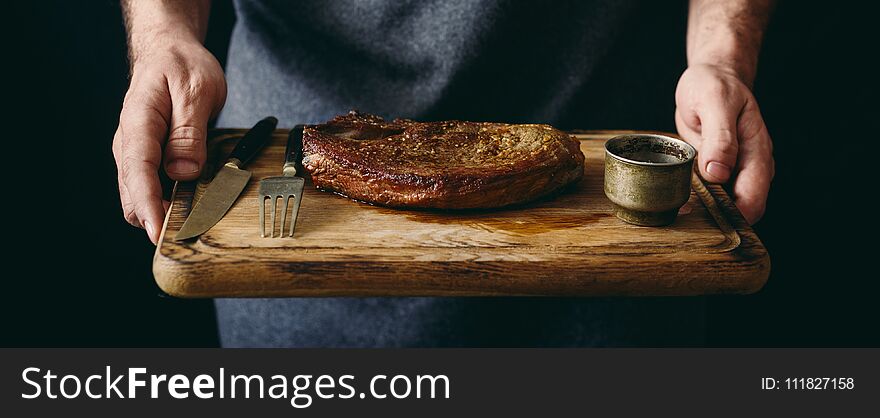 Man holding grilled beef steak with spices on cutting board