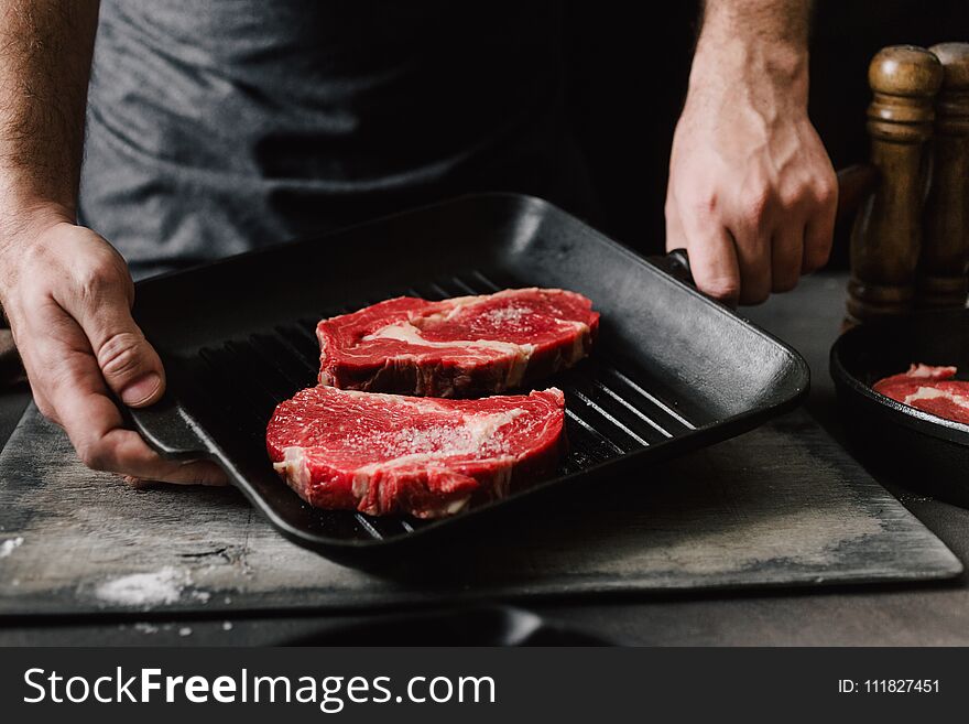 Male hands holding grill pan beef steaks Man cooking