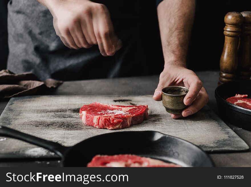 Male hands sprinkle salt beef steaks on the home kitchen
