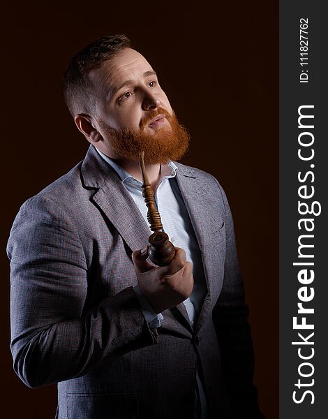 Portrait of a red bearded man smoking a pipe on a brown background