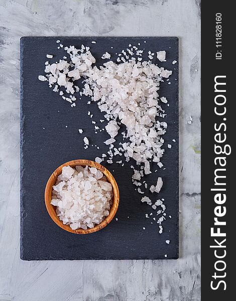 Large white sea salt in a natural wooden bowl on dark board over lifgt background, top view, close-up, selective focus