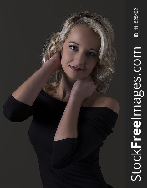 Beautiful blond woman in black top in dark with selective lighting and hands in hair