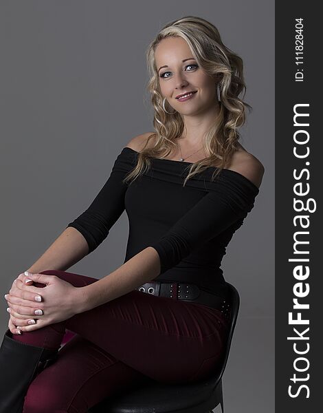 Beautiful blond woman in curly hair and black top and red pants on a grey background