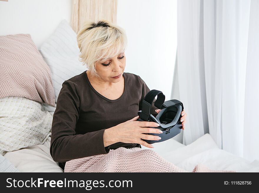 An elderly woman is going to put on virtual reality glasses to use them to immerse in the virtual world. The older generation and new technologies