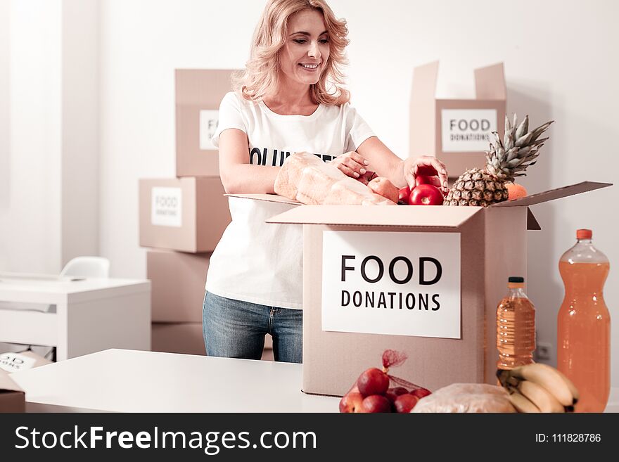Collect everything. Busy female keeping smile on her face and bowing head while controlling process of food donations. Collect everything. Busy female keeping smile on her face and bowing head while controlling process of food donations