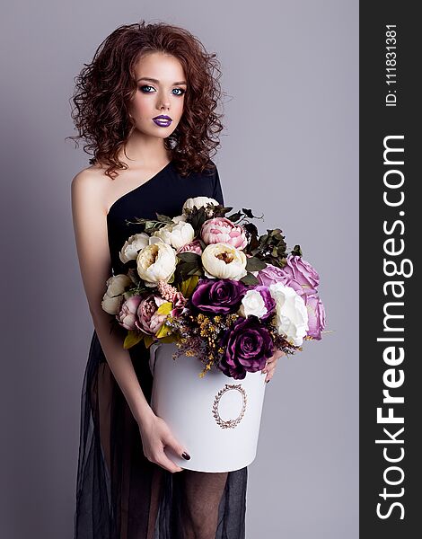 Beautiful girl with plump lips in black body with a bouquet of flowers in the studio, evening hairstyle and makeup