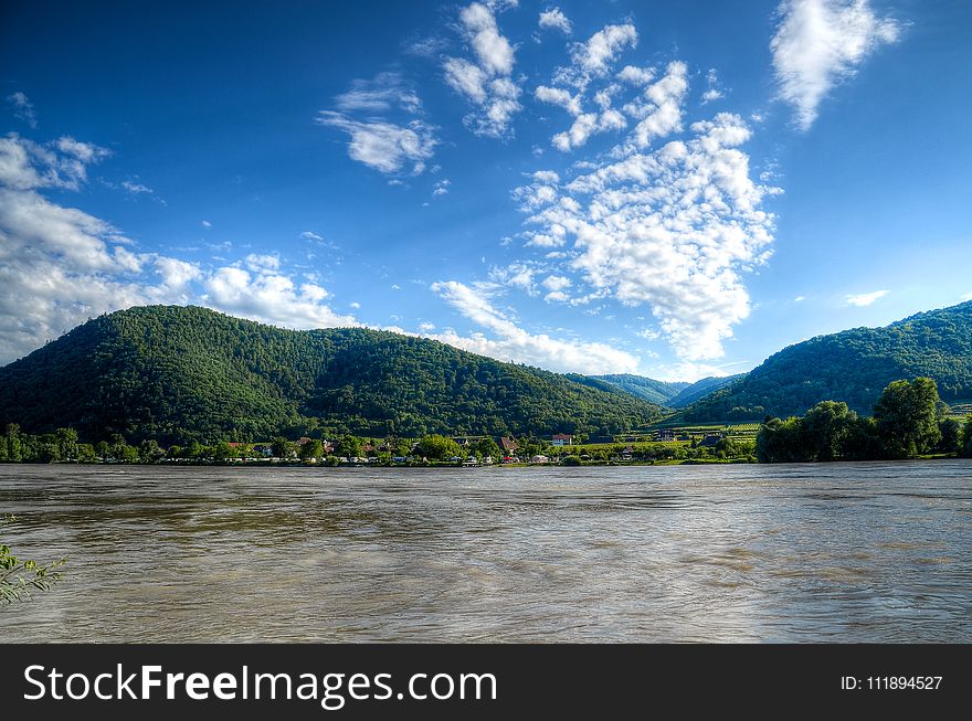 Body Of Water Near Mountains Under Blue Sky