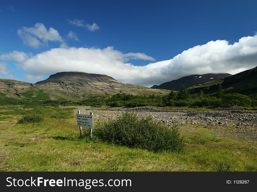 Landscape photo of a valley in a clear weather, sign on ground says, no camping, fishing area