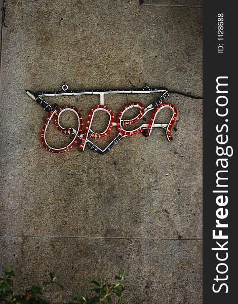 A neon open sign on a stone wall background.