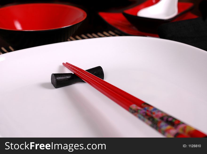 Red chopsticks on white plate with soup spoon and rice bowl