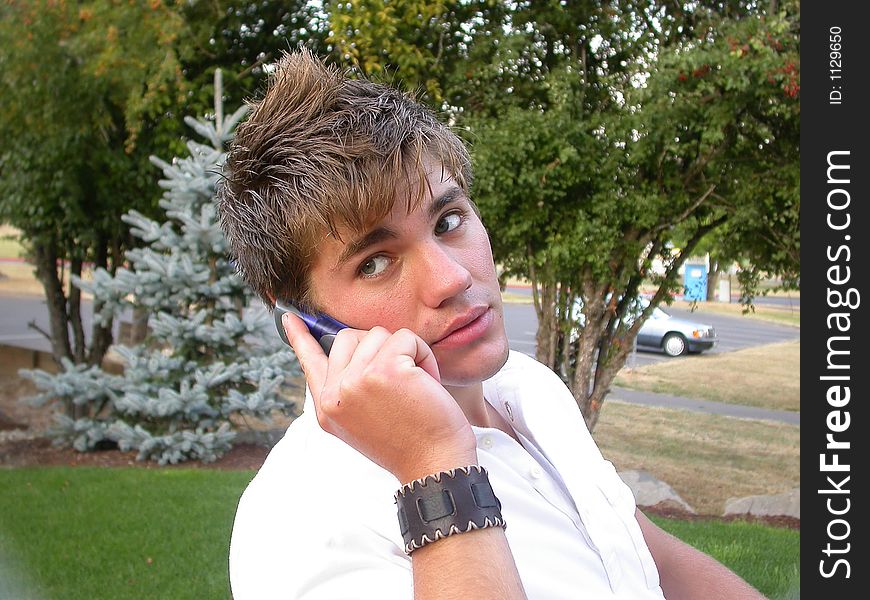 A young man looks at the camera while talking on his cell phone. A young man looks at the camera while talking on his cell phone