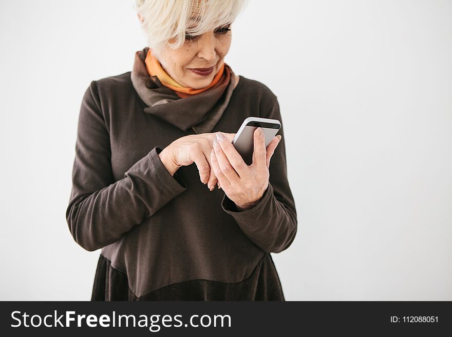 A positive modern elderly woman is holding a cell phone and is using it. The older generation and modern technology.
