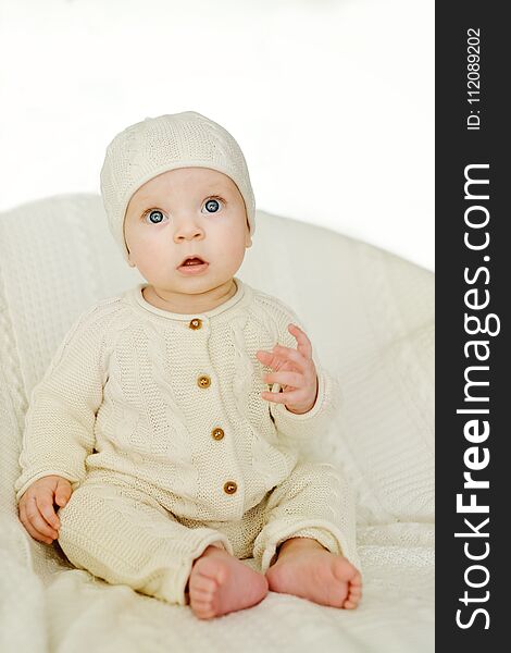 Sweet baby wearing knitted suit is sitting on the chair