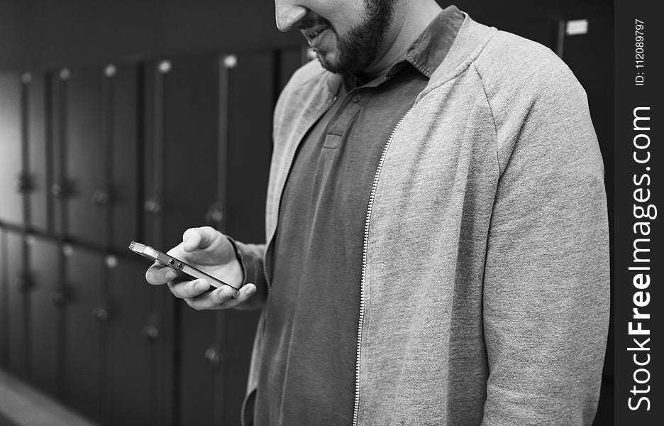 Grayscale Photo of Man Wearing Zip-up Jacket Holding Android Smartphone