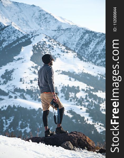 Man Wearing Gray Long-sleeved Shirt And Brown Shorts Holding Black Dslr Camera On Mountain