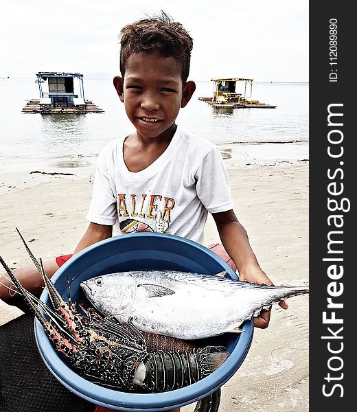 Boy Wearing White Crew-neck T-shirt Holding Blue Plastic Basin Full of Lobster and Fish