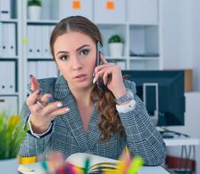 Young Serious Caucasian Businesswoman Sitting At Desk In Office, Speaking On The Phone And Pointing At Te Camera. Royalty Free Stock Image