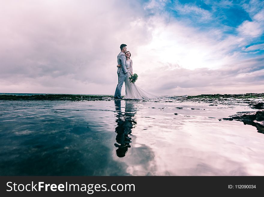 Man in Gray Dress Suit Jacket Embraces Woman Wearing Wedding Gown