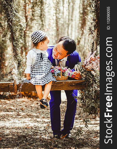 Selective Focus And Color Photography Of Man Looking At Her Girl Sitting On Garden Swing White Holding Bouquet Of Flower In Brown