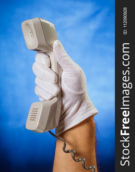 Male hand in white glove holding landline phone receiver over blue background