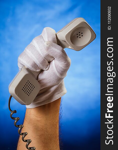 Male hand in white glove holding landline phone over blue background