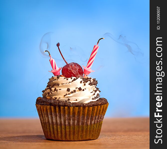 Birthday cupcake with blown out candles over bluye background