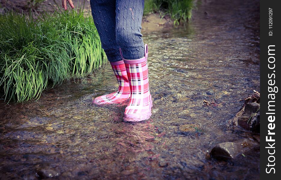 A young child wades through a spring creek in pink plaid rubber boots. A young child wades through a spring creek in pink plaid rubber boots