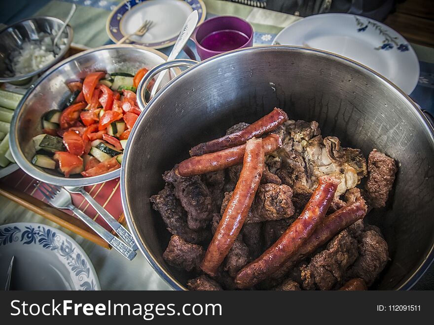 A pot full of barbecued sausages and other meat and a salad. A pot full of barbecued sausages and other meat and a salad