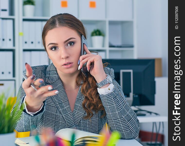 Young businesswoman sitting at desk in office, listening on the phone. Young businesswoman sitting at desk in office, listening on the phone.