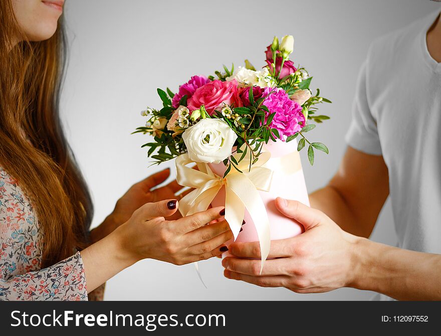 The guy gives a bouquet of flowers to a girl. Composition of flowers in a pink hatbox. Tied with wide white ribbon and bow.
