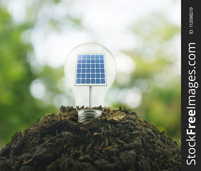 Light bulb with solar cell inside on pile of soil over green environment