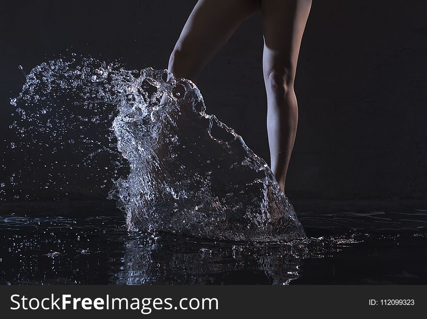 Barefoot slender woman dancing in water in dark room cropped shot. Barefoot slender woman dancing in water in dark room cropped shot