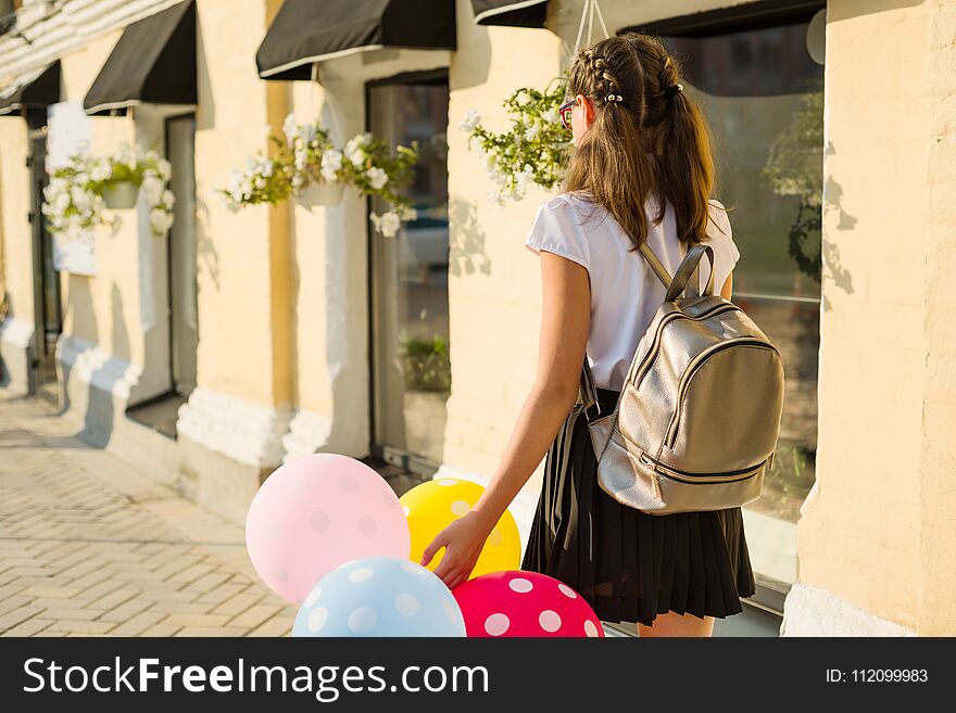 Back view. Girl teenager high school student with balloons, in school uniform goes along the city street