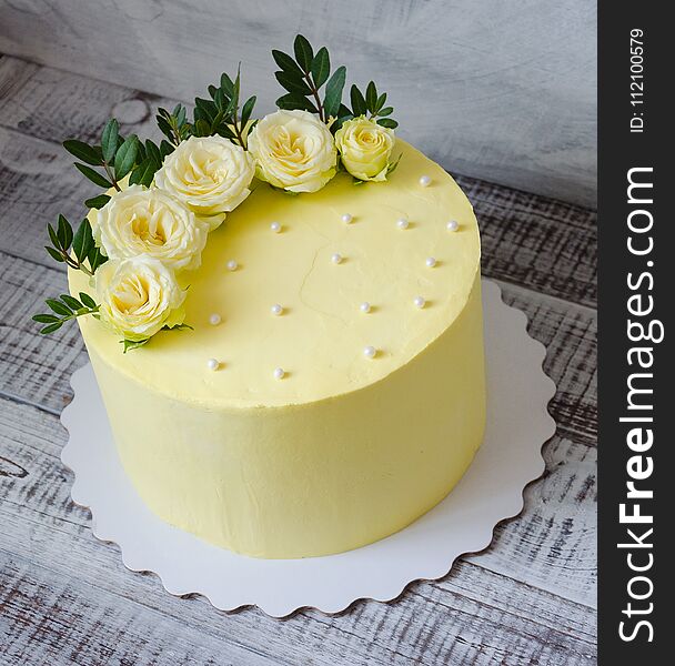 A yellow cream cheese cake with roses and greenery