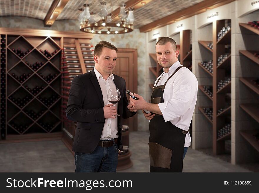 Two Young Professional Sommeliers Choosing Wine In Wine Cellar