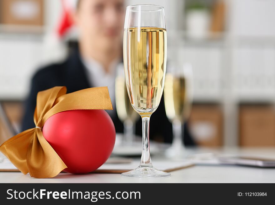 Businessman in santa hat against a background of a glass with champagne and ball decorating a Christmas tree