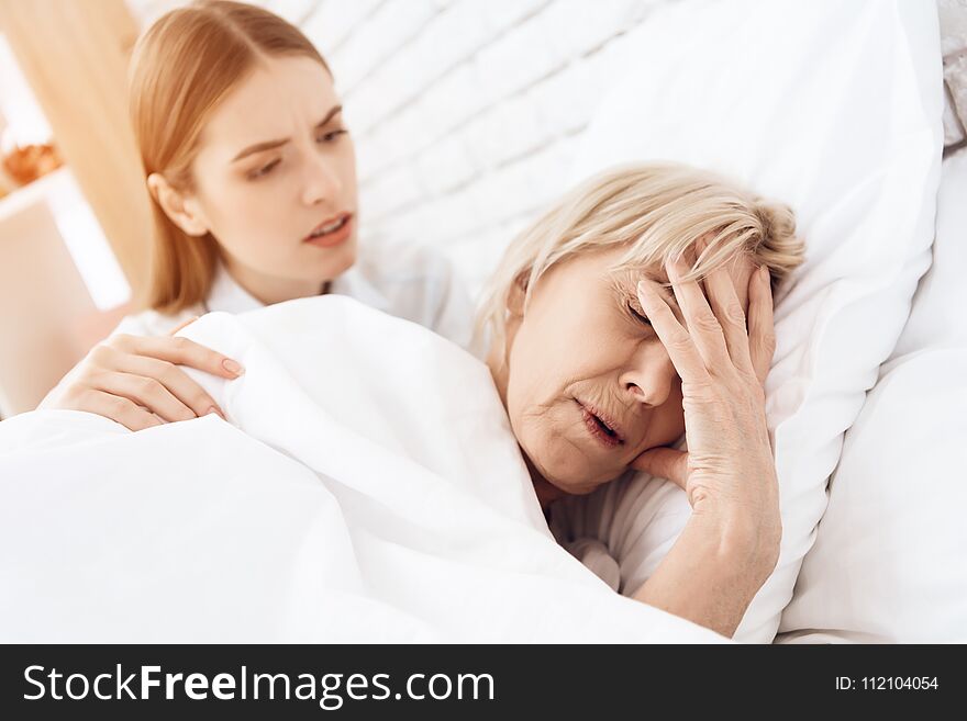 Girl is nursing elderly women in bed at home. Woman is feeling bad, girl is concerned.