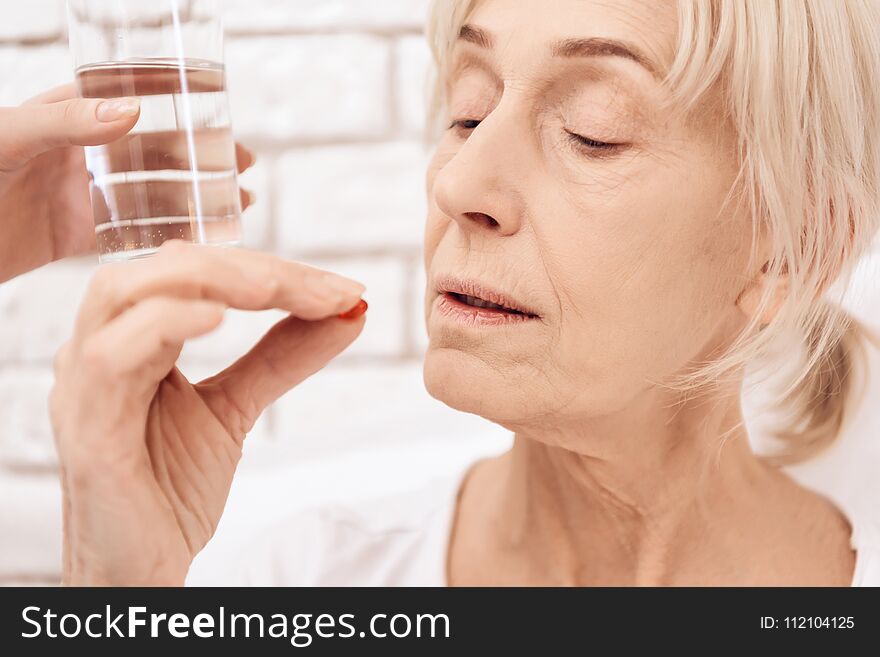 Girl is nursing elderly woman in bed at home. Girl brings water and pills.