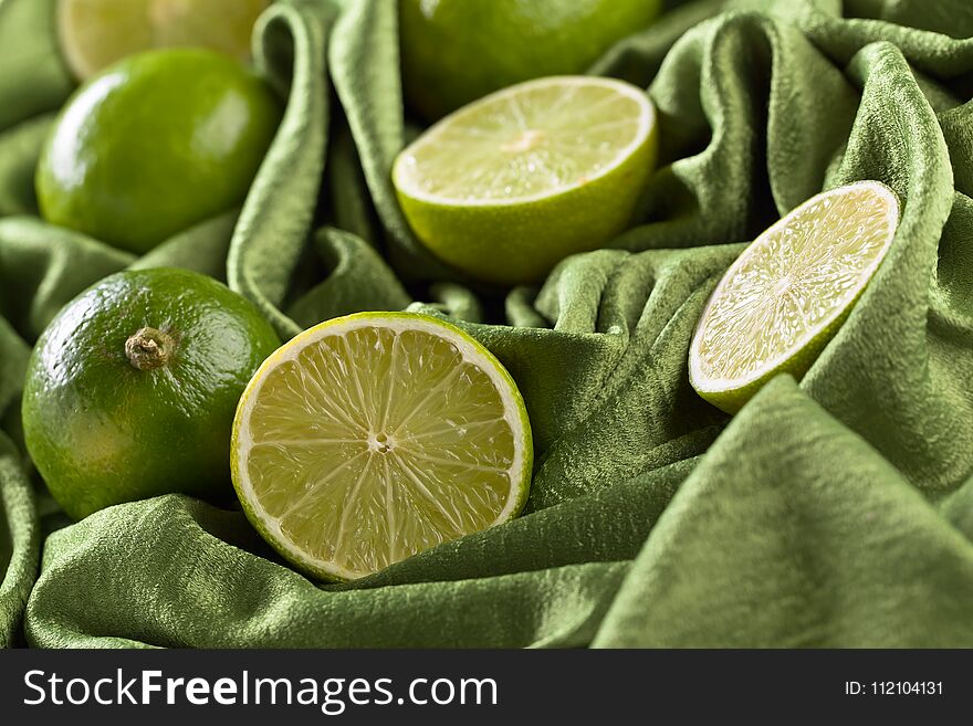 Group of whole and cut fresh limes on a green satin